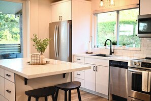 Eine moderne Küche mit einem Edelstahl-Kühlschrank, einer Spülmaschine und einem Backofen. Ein Fenster bietet Blick auf Grünflächen.