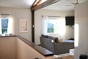 Ein modernes Wohnzimmer mit einer Couch, einem Flachbildfernseher und einem Fenster mit Vorhängen.