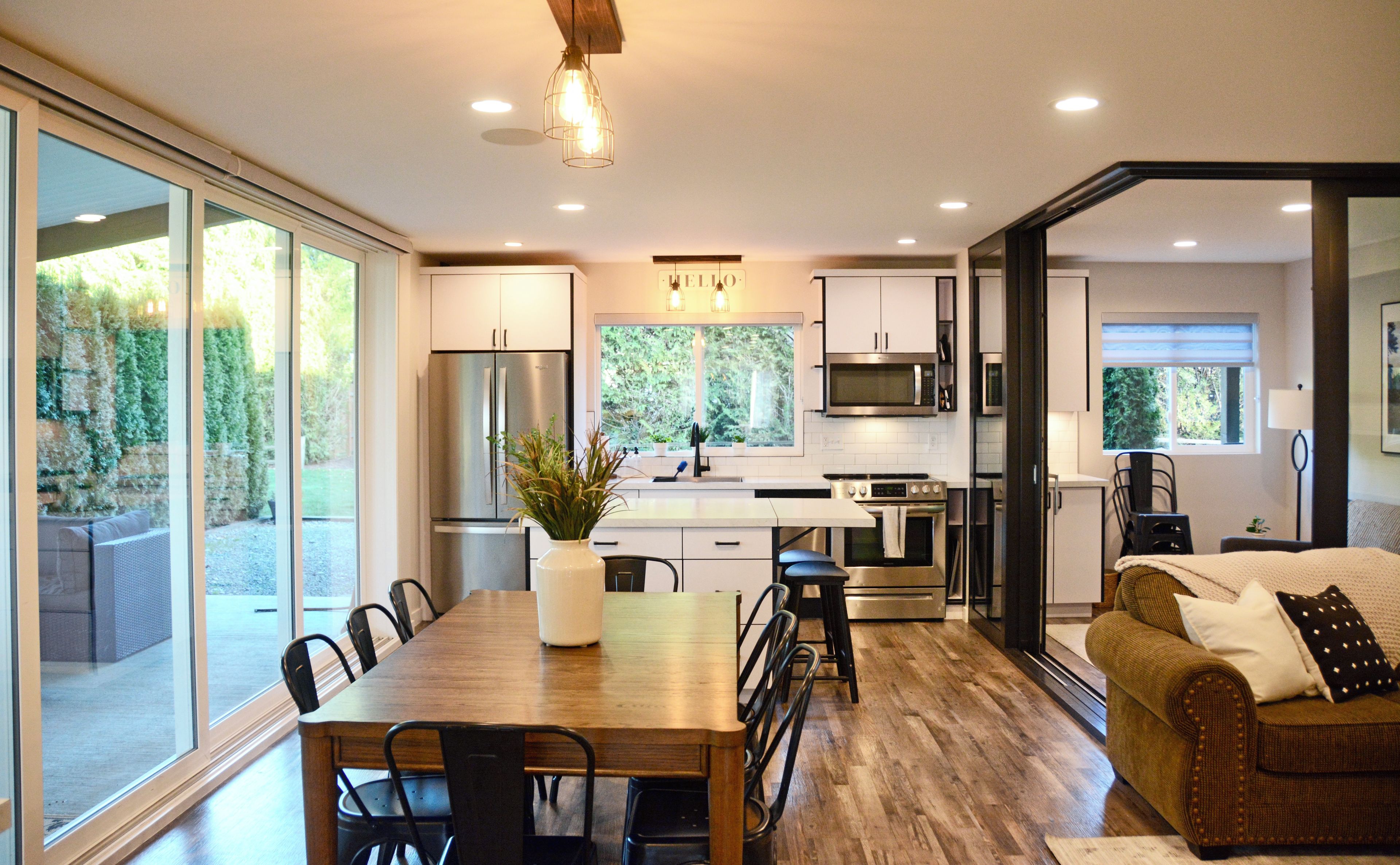 A modern kitchen with a central island, stainless steel appliances, and a view of greenery outside.