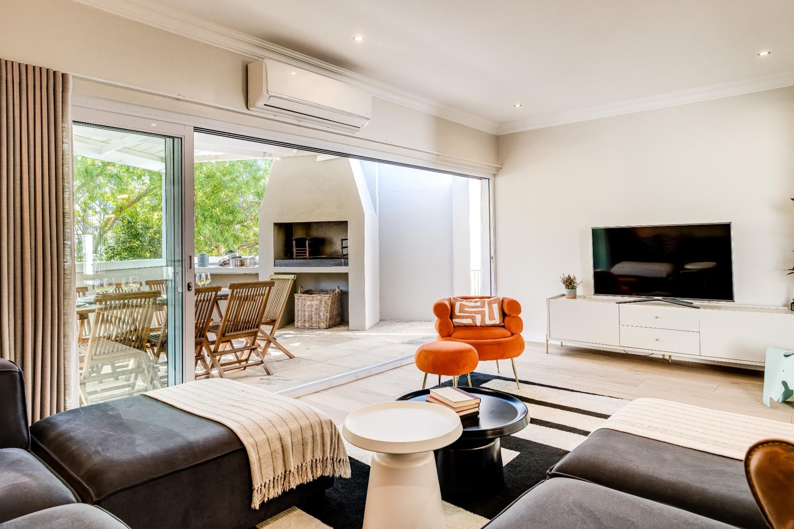 Un salon moderne avec un canapé, un pouf et un téléviseur posé sur un meuble blanc.