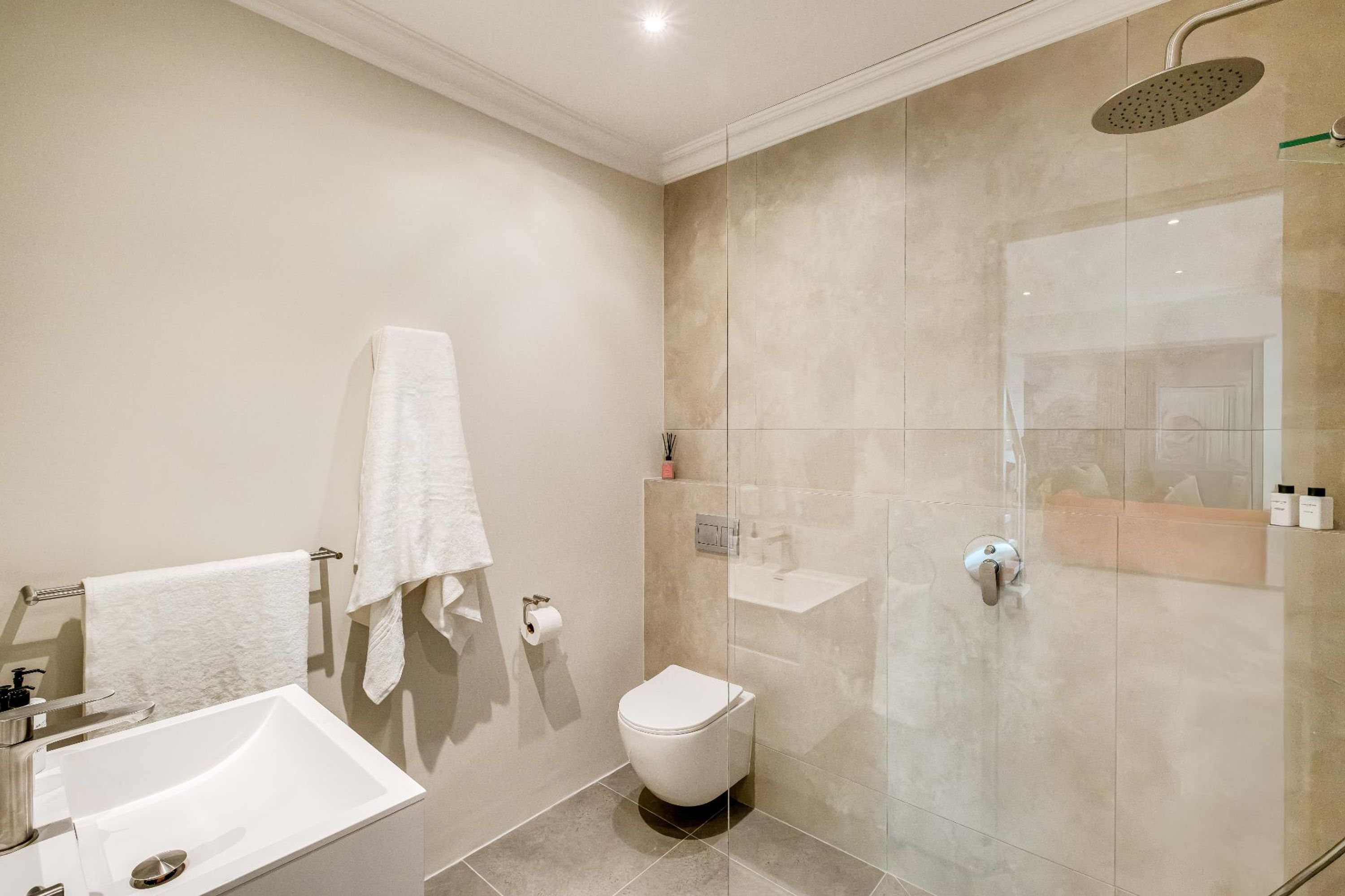 Un baño moderno con ducha envuelta en vidrio, inodoro blanco y lavamanos con espejo.