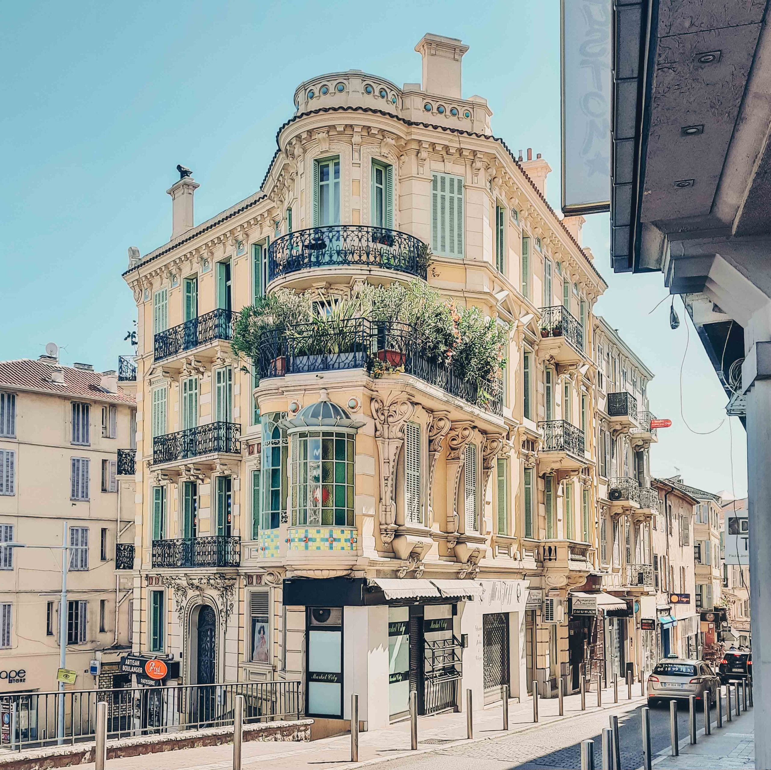 A multi-story building with ornate balconies, a café on the ground floor, and a clear sky.