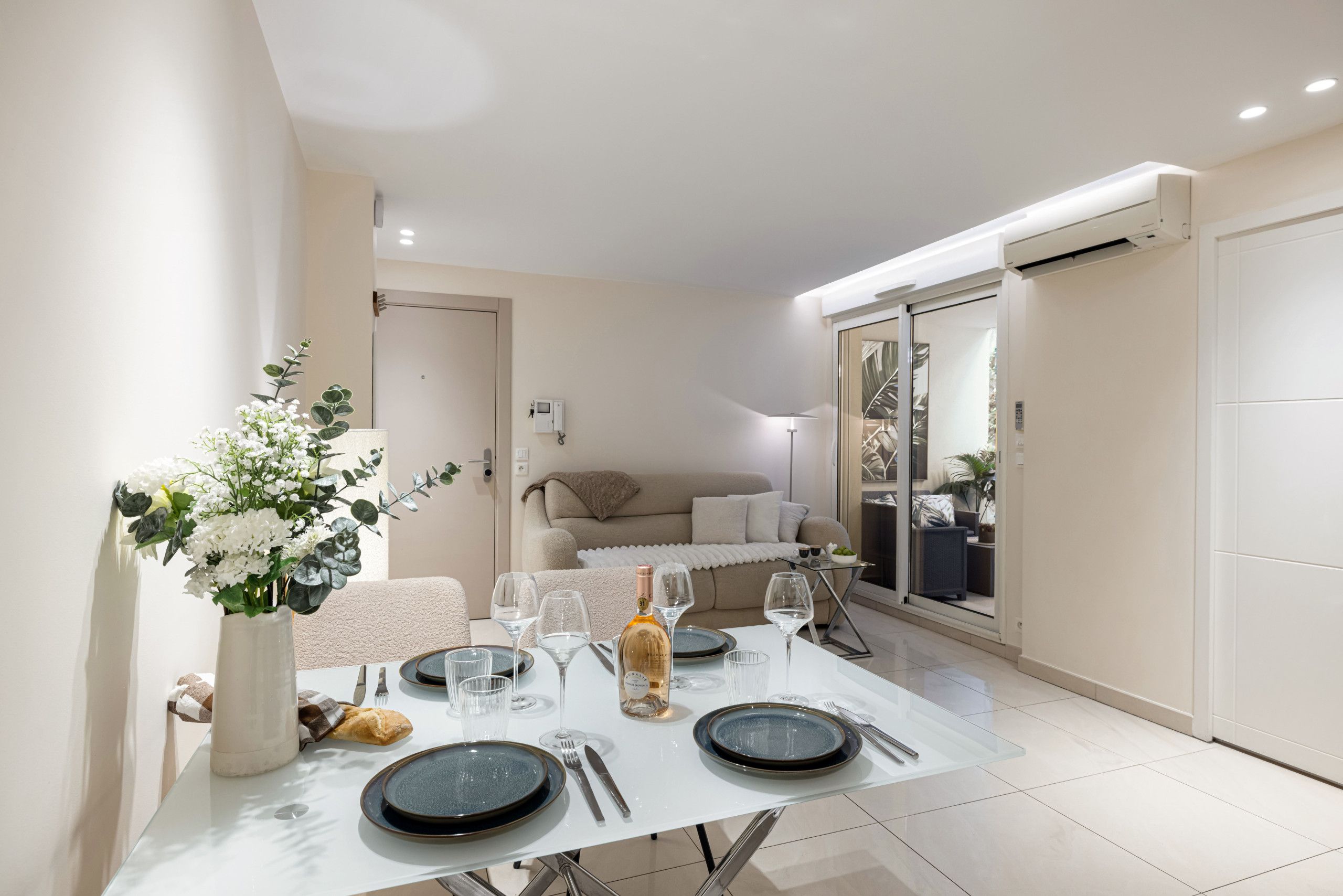 A dining area with a table set for four, a vase of flowers, and a bottle of wine.