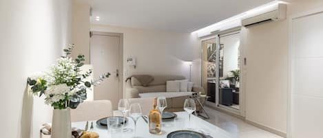 A dining area with a table set for four, a vase of flowers, and a bottle of wine.