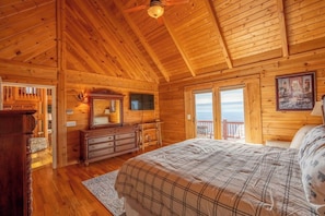 Ein Schlafzimmer einer Holzhütte mit Bett, Kommode und großem Fenster mit Aussicht.