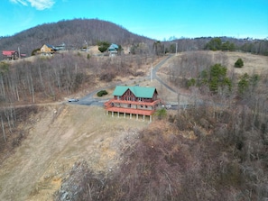 Ein Chalet mit roter Fassade und grünem Dach, umgeben von einer hügeligen Landschaft mit vereinzelten Bäumen.