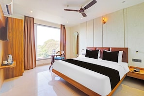 Une chambre d’hôtel avec un grand lit, un ventilateur de plafond, une fenêtre avec des rideaux, une table de chevet avec une lampe et un téléphone fixé au mur.
