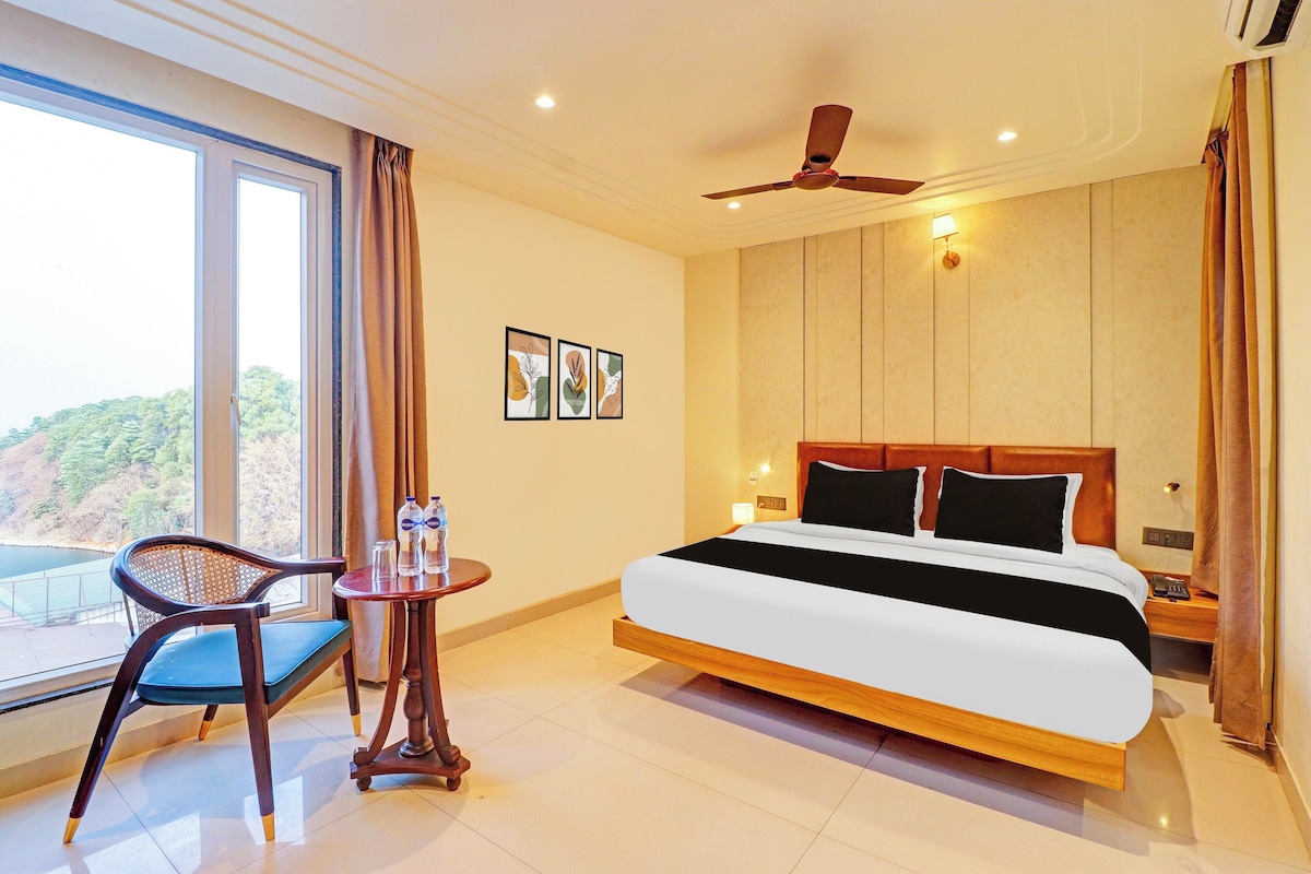 Une chambre d’hôtel avec un lit, une chaise, une petite table avec des bouteilles d’eau, un ventilateur de plafond et une vue sur l’extérieur.