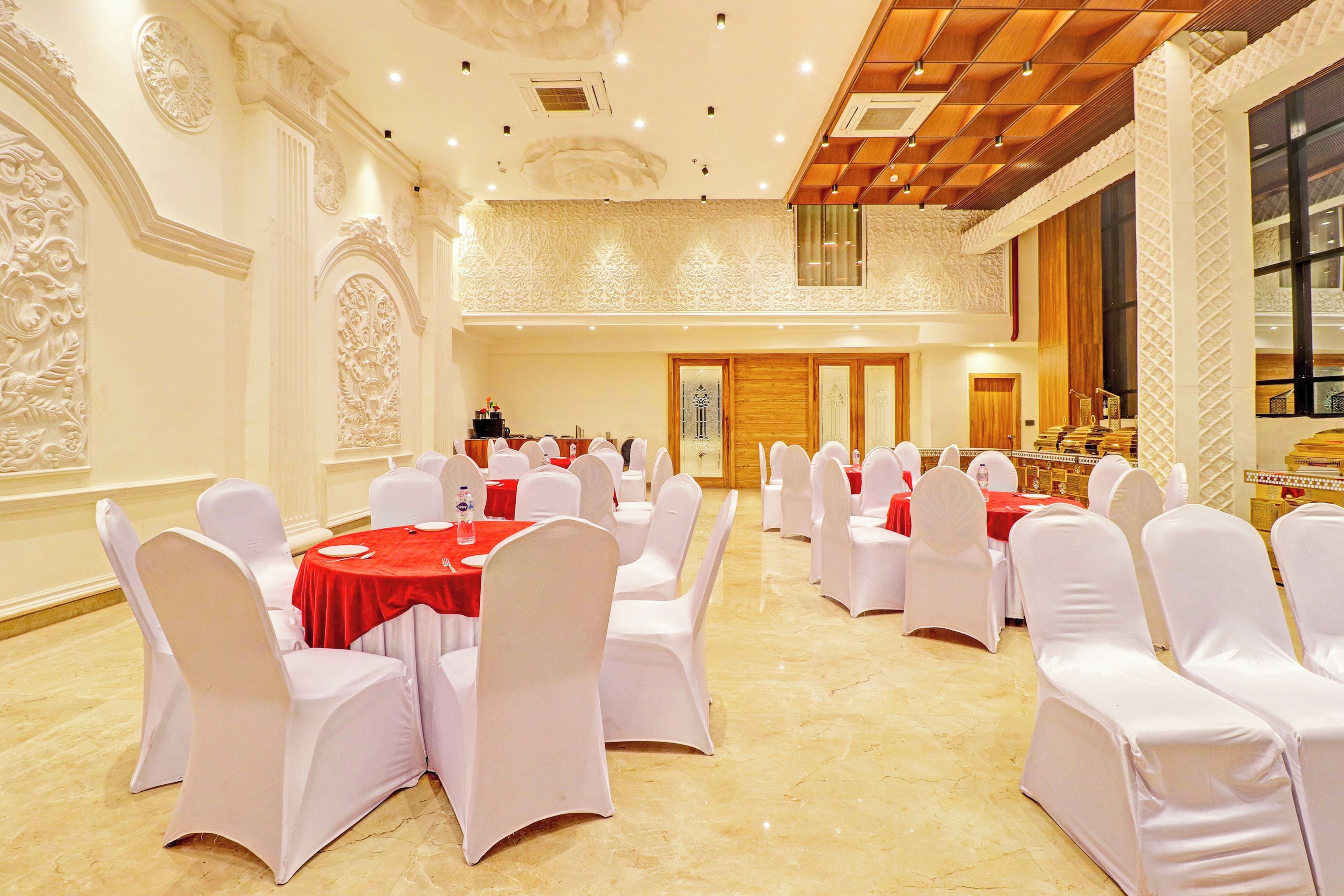 A banquet hall with round tables, white chairs, and red tablecloths.