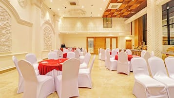 A banquet hall with round tables, white chairs, and red tablecloths.