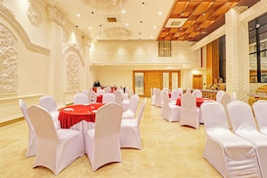 Un salón de banquetes con mesas redondas, sillas blancas y manteles rojos.