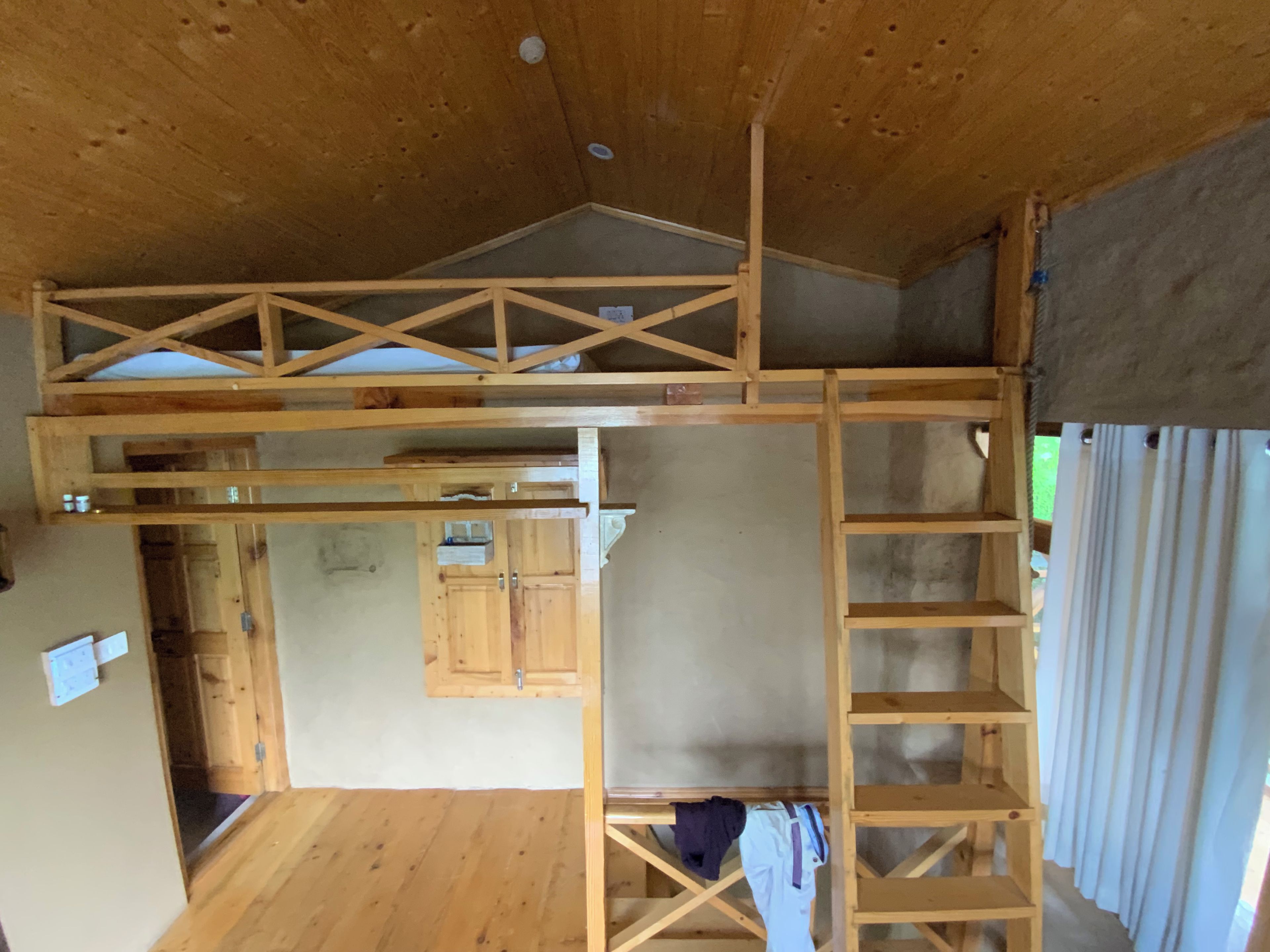 Een kamer met houten plafond, een vide met een houten ladder, en een keuken met kastjes.