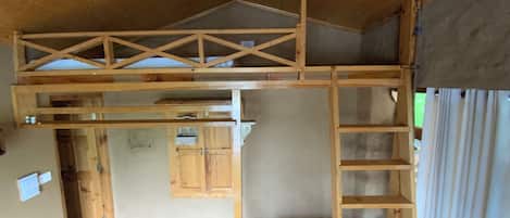 Una habitación con techo de madera, un área en alto con escalera de madera y una cocina con armarios.