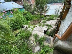 A garden with stone steps leading to a house with a metal roof. - Serene 1-bedroom cottage in charming Bashisht perfect for relaxing (Bashisht)