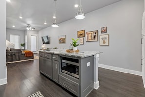 A modern kitchen with grey cabinetry, a marble countertop, and overhead lighting.
