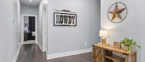 En gang med et skilt der siger 'HOWDY', en stjerndekoration og et træbord med en lampe og en plante.