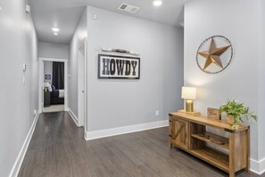 Ein Flur mit einem Schild, auf dem 'HOWDY' steht, einer Stern-Dekoration sowie einem Holztischchen mit einer Lampe und einer Pflanze.