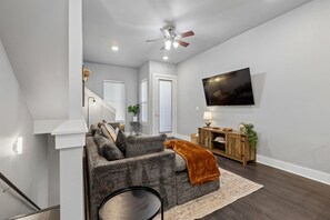 A modern living room with a grey sofa, a wooden cabinet, and a flat-screen TV mounted on the wall. - 4 Bd 3 Bath | Near TCU Campus (Fort Worth)