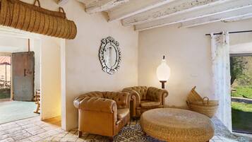 A room with a patterned floor, two leather sofas, a woven pouf, a wall-mounted mirror, and a hanging basket.