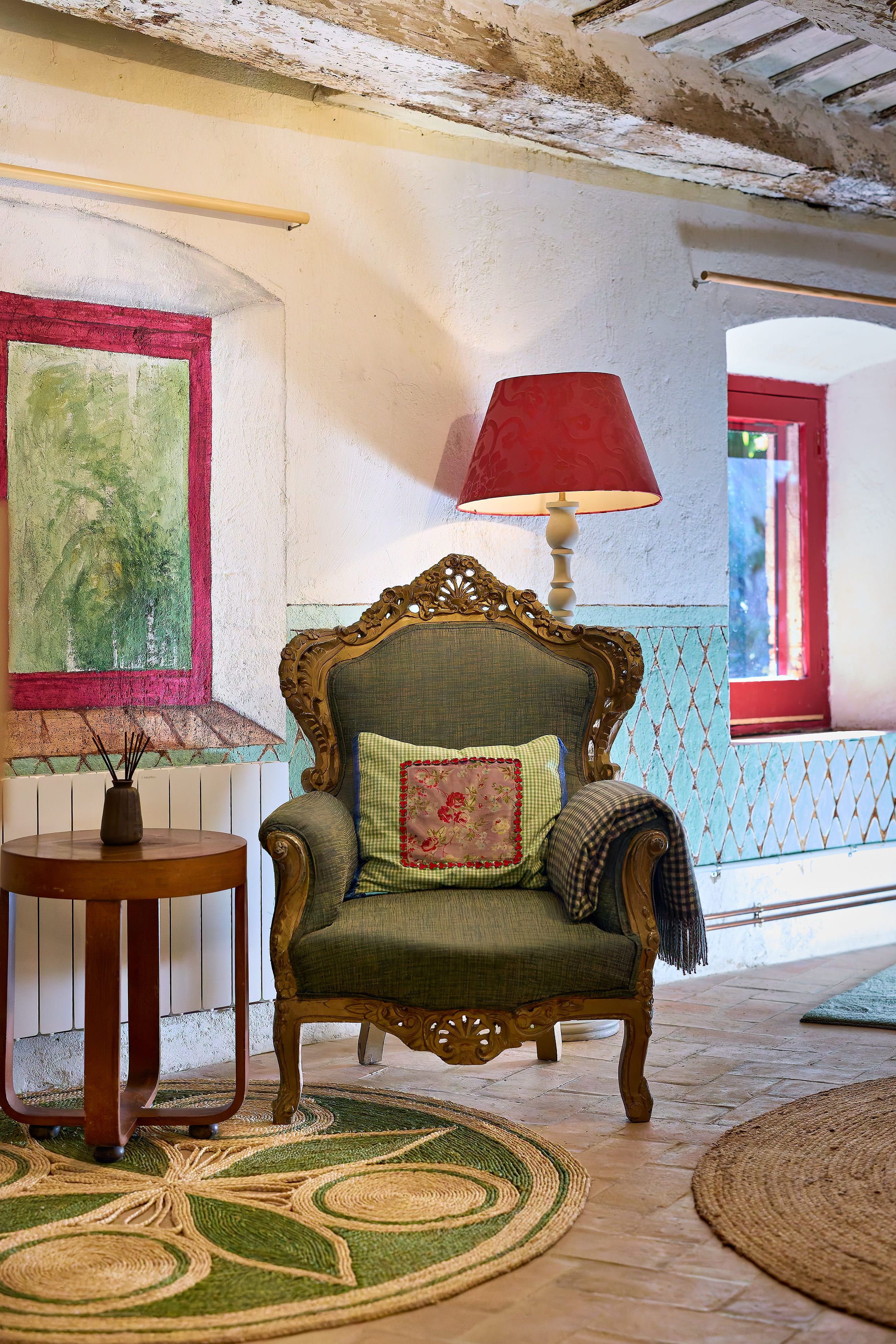 A room with a vintage armchair, a table with a vase, and a lamp.