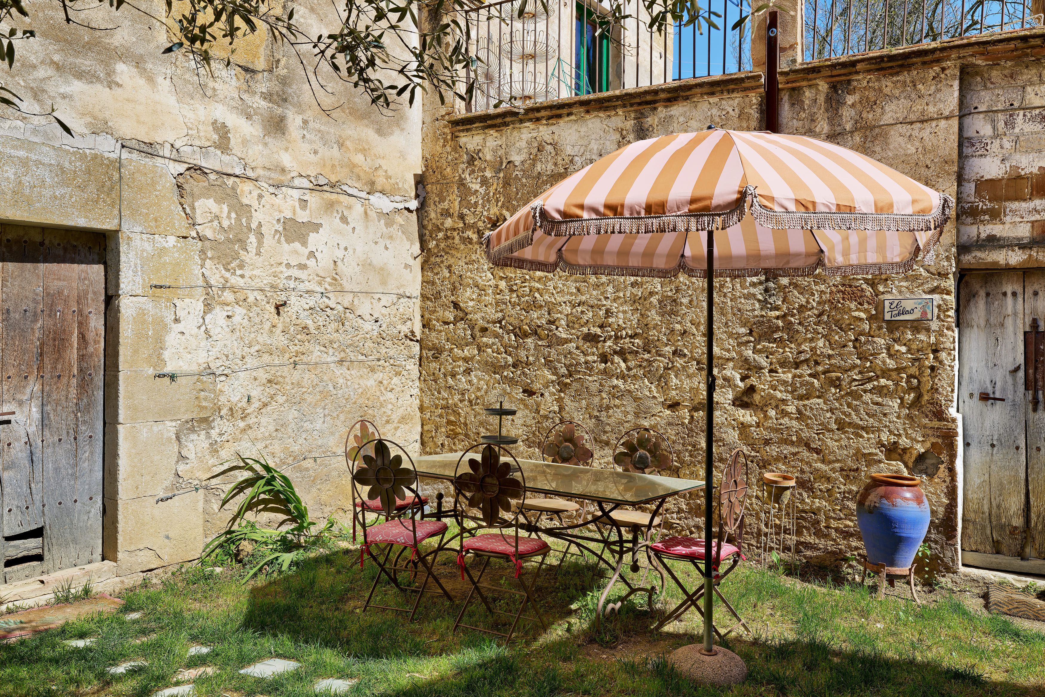 A rustic outdoor seating area with a table and chairs, a striped umbrella, and a decorative vase.