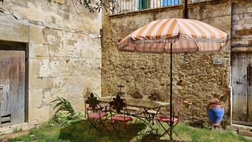 A rustic outdoor seating area with a table and chairs, a striped umbrella, and a decorative vase.