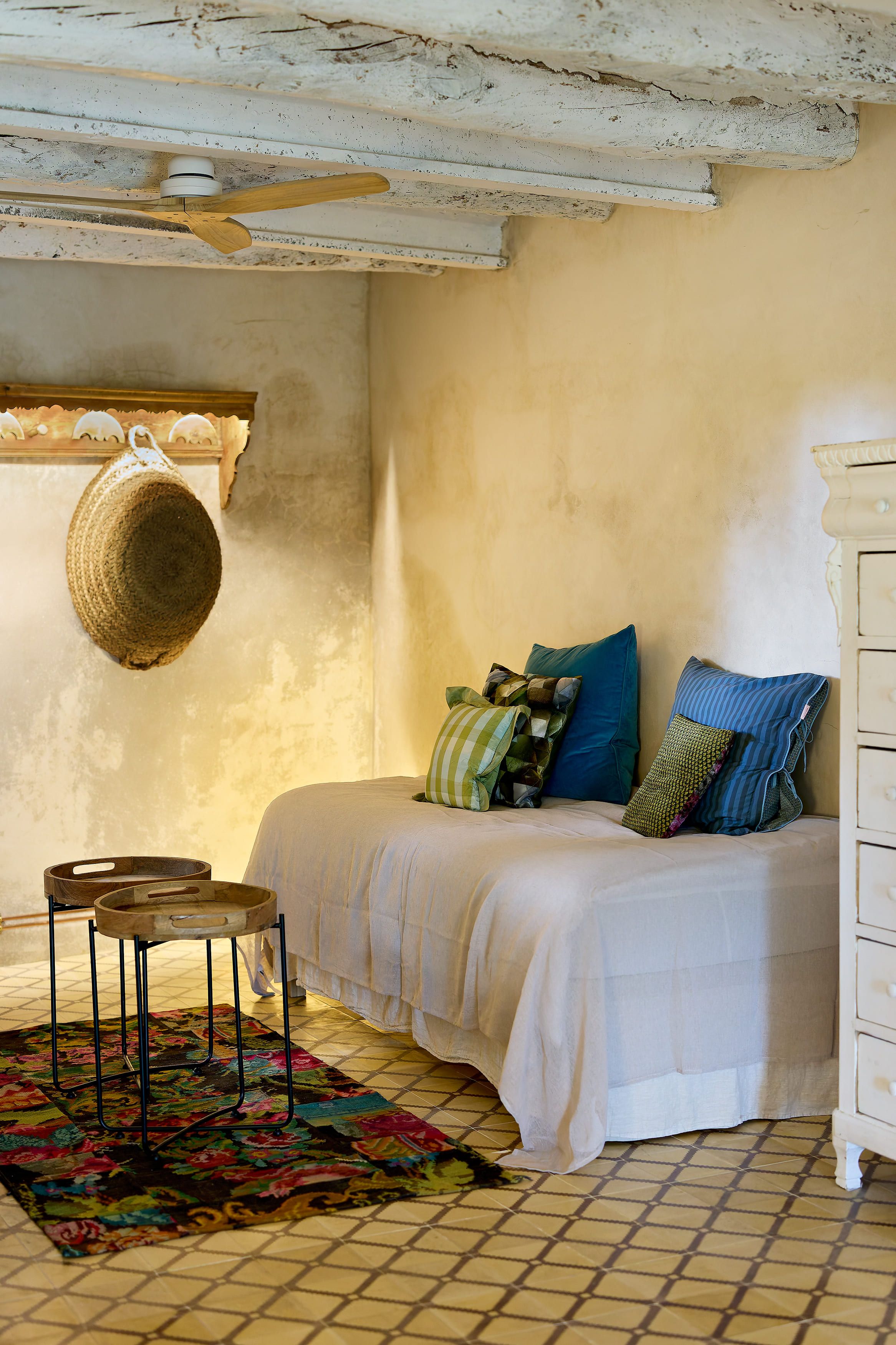 A bedroom with a bed, a hanging basket, a small table, and a colorful rug.