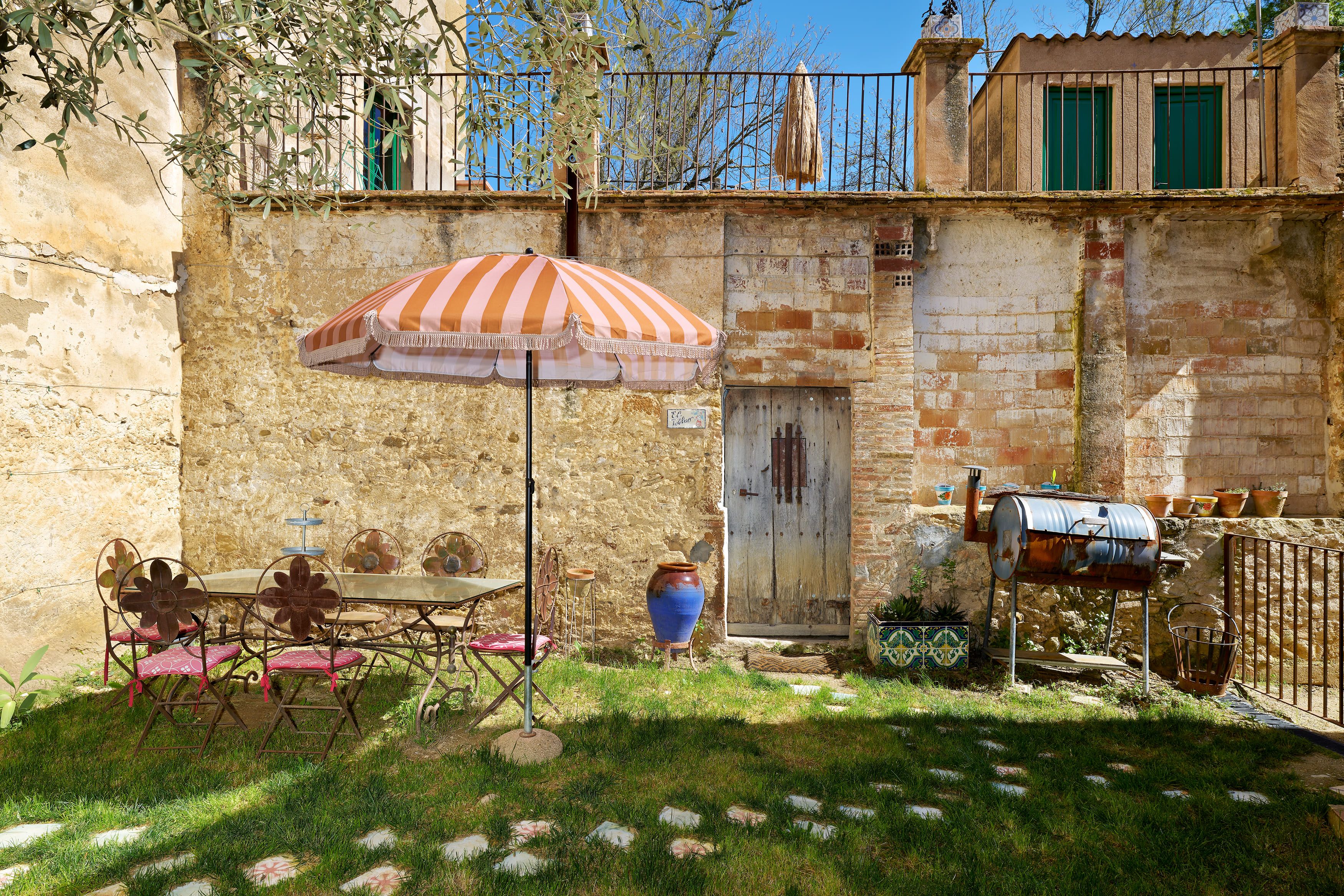 An outdoor patio with a table and chairs, a large striped umbrella, and a rustic stone wall.