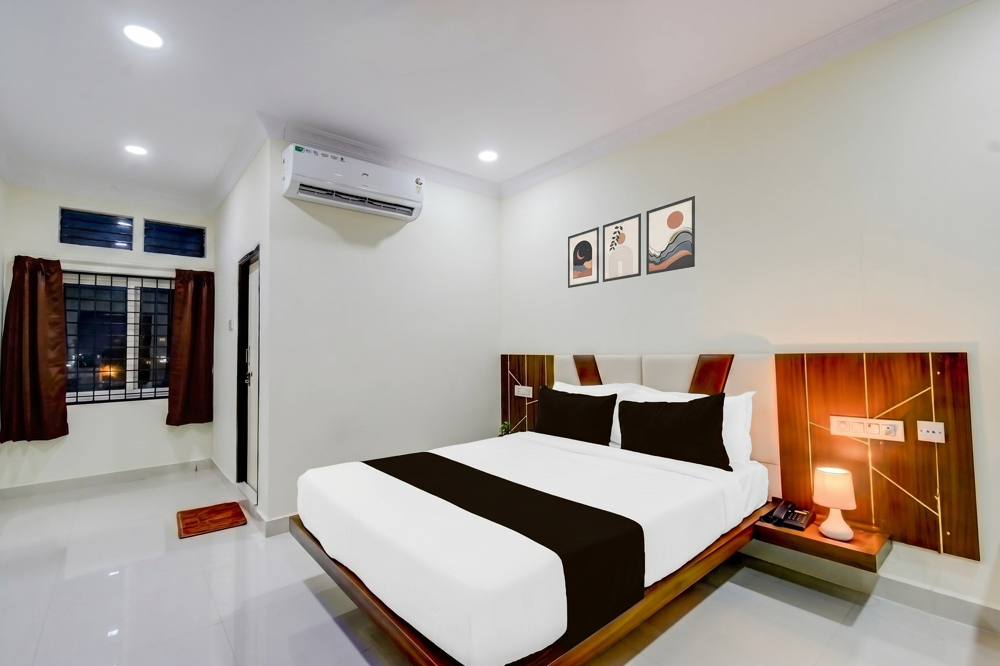 A hotel room with a large bed, a bedside table with a lamp, and a wall-mounted air conditioner.