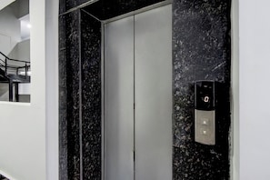 Un ascensor con un panel de control en la pared, una pared de mármol y una escalera a la izquierda.