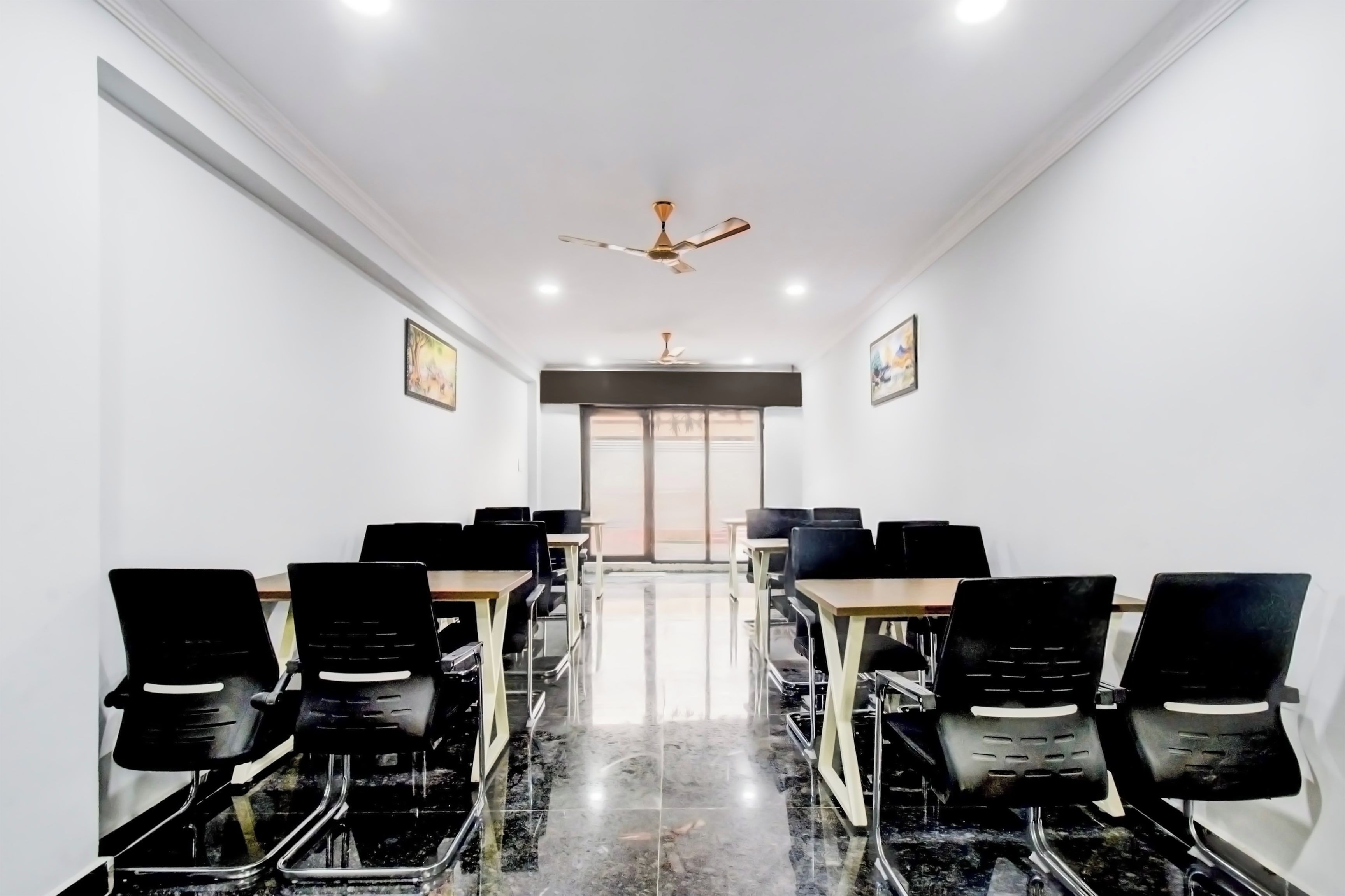 A conference room with a long table, black chairs, a ceiling fan, and two framed pictures on the walls.