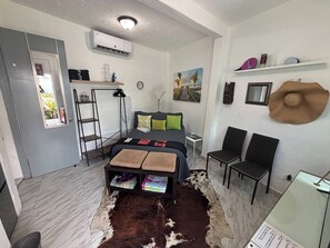 Ein gemütlicher Raum mit einem Bett, einem kleinen Schreibtisch, einem Stuhl, einem Regal mit Gegenständen und einem Kuhfellteppich.