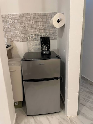 Eine kompakte Küchenzeile mit einem Galanz-Kühlschrank, einer Kaffeemaschine und einer Toilettenpapierrolle an der Wand.