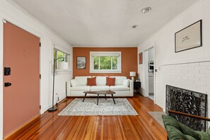 A living room with a white sofa, a coffee table, a patterned rug, and a fireplace. - Cozy Broad Ripple Bungalow | Walk to Everything (Indianapolis)