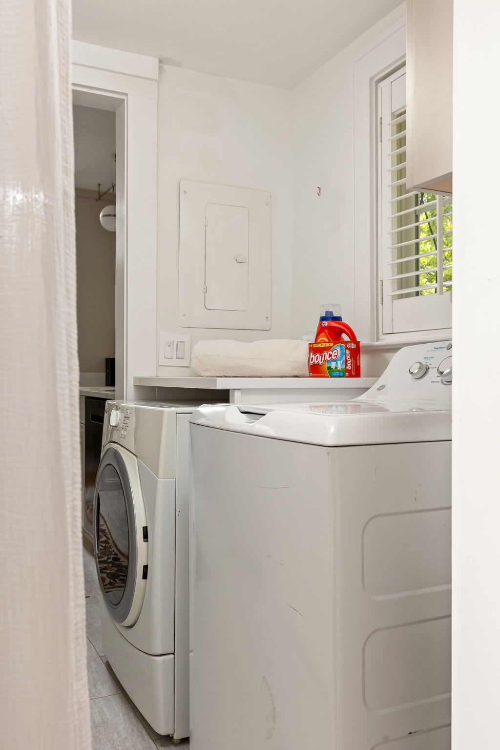 Une buanderie équipée d’un lave-linge, d’un sèche-linge et d’une bouteille de lessive Bounce posée sur une étagère.