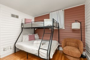 A bunk bed with white bedding and pink pillows, a brown chair, and a wall-mounted lamp. - Cozy Broad Ripple Bungalow | Walk to Everything (Indianapolis)