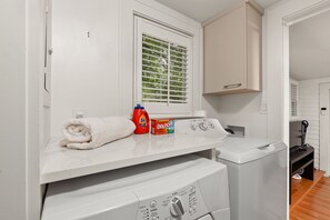 A laundry room with a washing machine, dryer, and a window with blinds. - Cozy Broad Ripple Bungalow | Walk to Everything (Indianapolis)