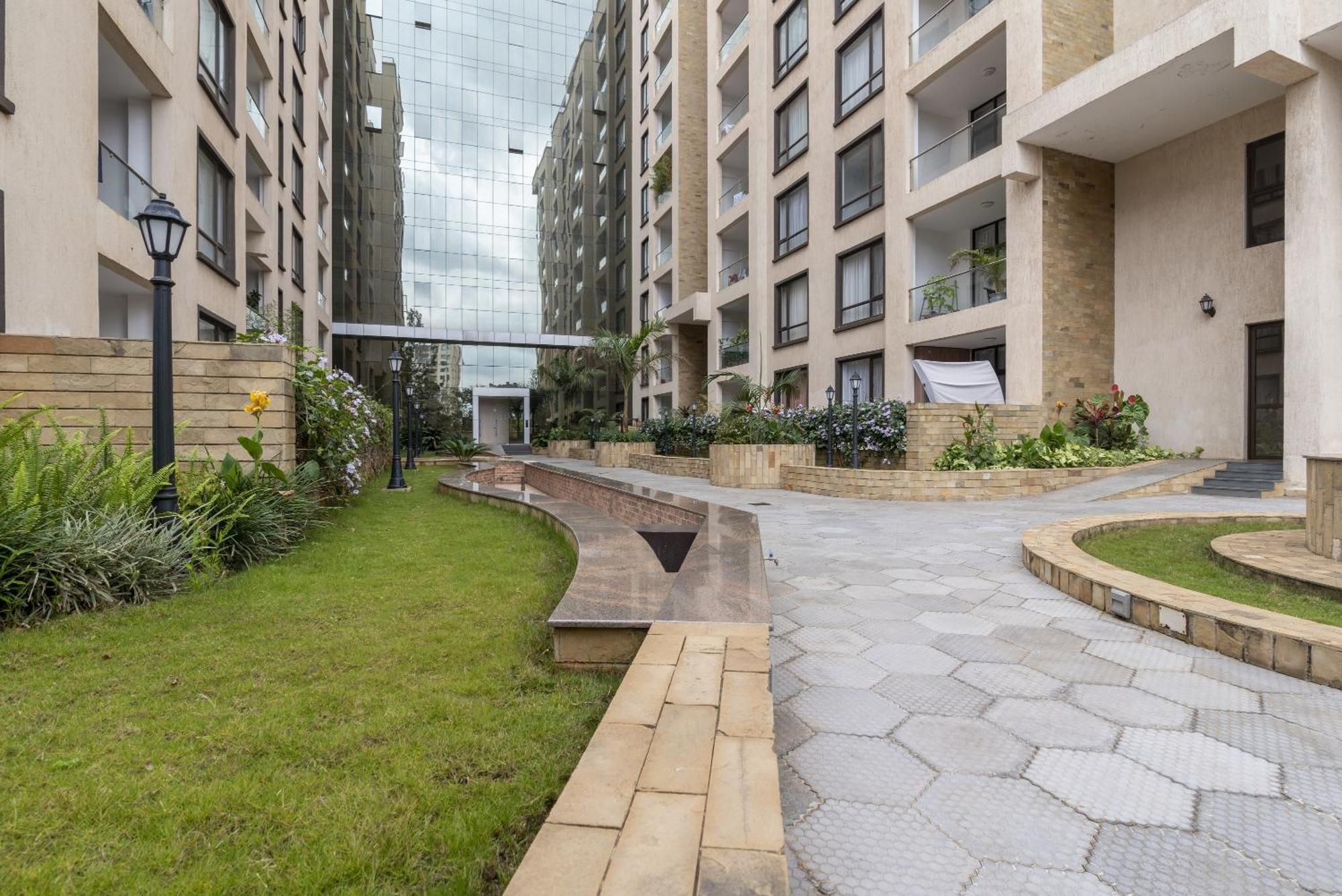 Un immeuble résidentiel moderne doté d’une cour intérieure, comprenant un chemin, des espaces verts et une façade en verre.