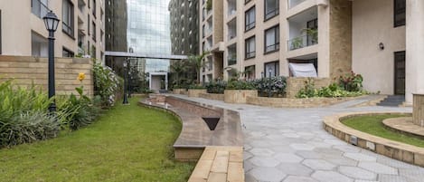 Un immeuble résidentiel moderne doté d’une cour intérieure, comprenant un chemin, des espaces verts et une façade en verre.