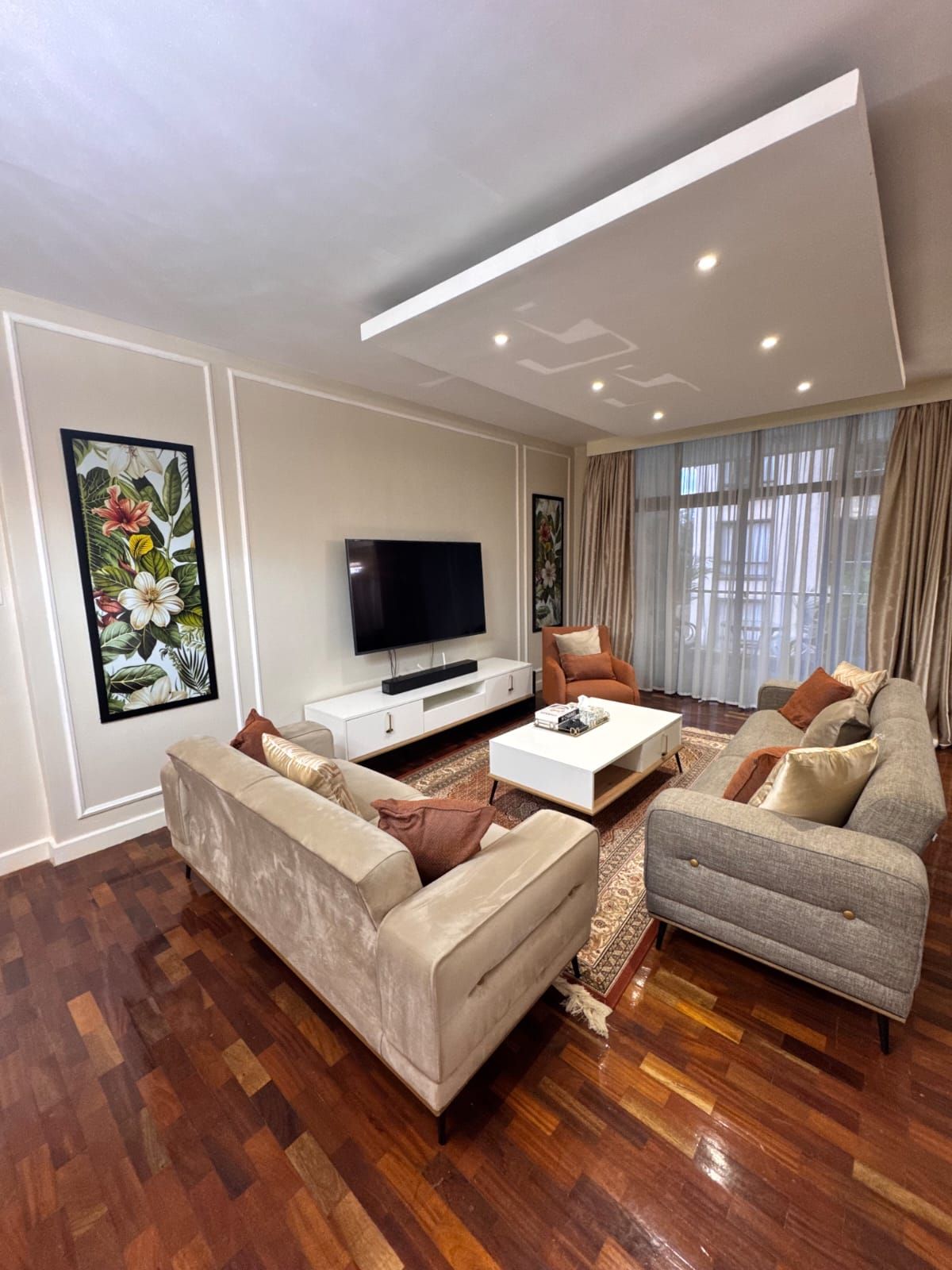 A modern living room with a flat-screen TV, two sofas, a coffee table, and artwork on the walls.