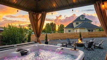 A hot tub under a wooden pergola with a view of a house and trees.