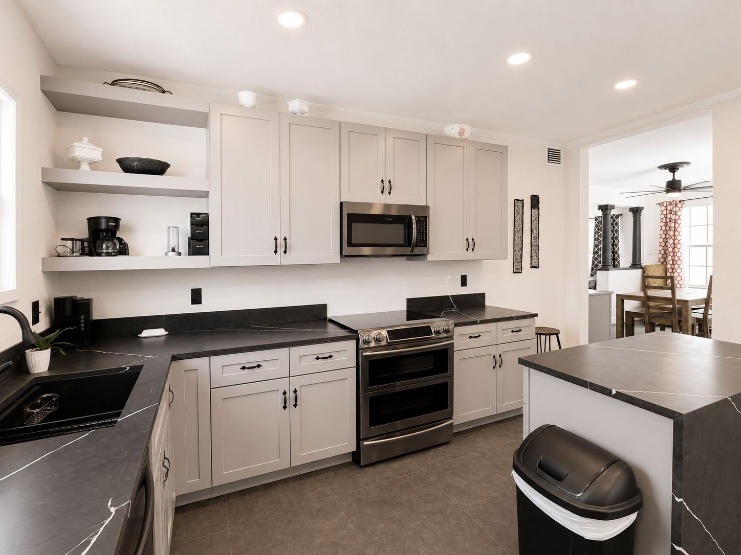 A modern kitchen with white cabinets, a black countertop, a built-in microwave, and an oven.