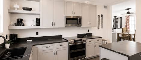 A modern kitchen with white cabinets, a black countertop, a built-in microwave, and an oven.