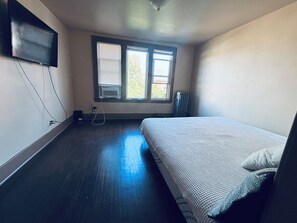 Ein Zimmer mit einem Bett, einem an der Wand befestigten Fernseher und einem Fenster mit Jalousien.