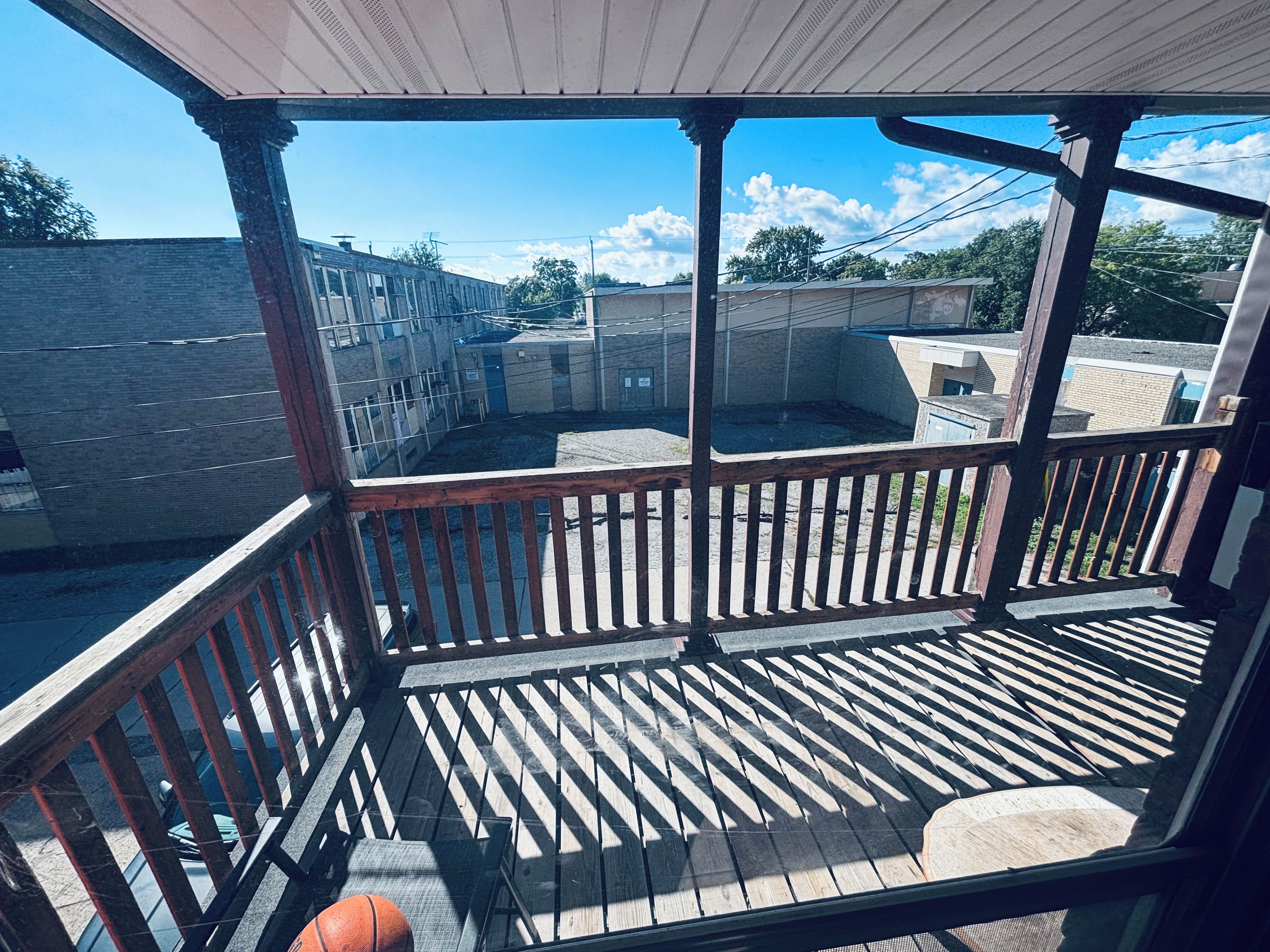 Ein überdachter Außenbereich mit Holzterrasse, einem Basketball und Blick auf ein Wohngebiet.