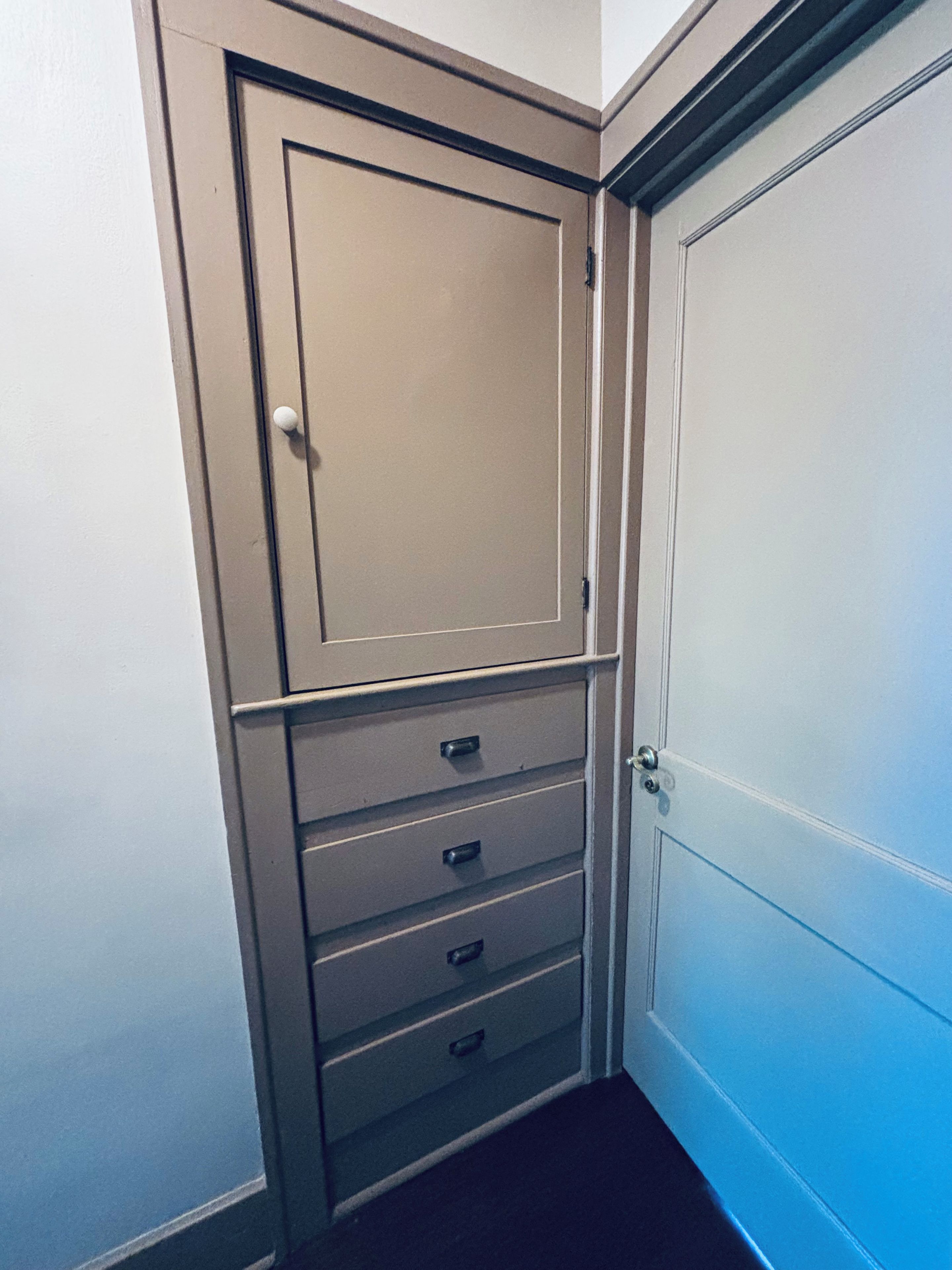 Ein Zimmer mit geschlossener Tür, einer Kommode und einem kleinen Fenster.