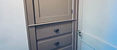 Una habitación con una puerta cerrada, un conjunto de cajones y un ventanal pequeño.