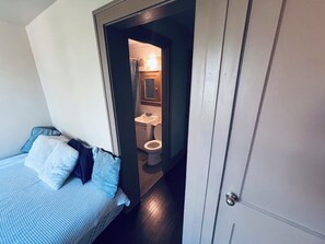 Ein Schlafzimmer mit Bett, Schrank und Blick in ein Badezimmer mit Toilette und Waschbecken.