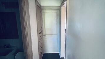 A narrow hallway with a door at the end, a light fixture on the ceiling, and a bathroom with a toilet and sink on the left.