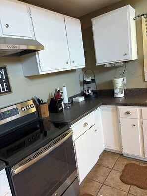 A kitchen with white cabinets, a stove, a coffee maker, and a clock.